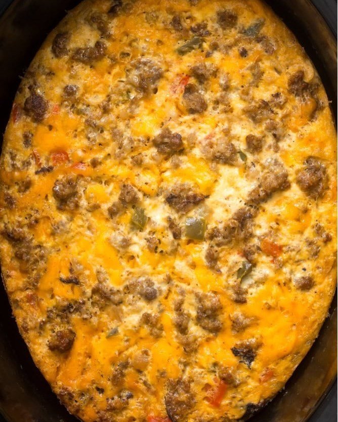 A cooked breakfast casserole with melted cheese, sausage, and peppers inside a slow cooker.