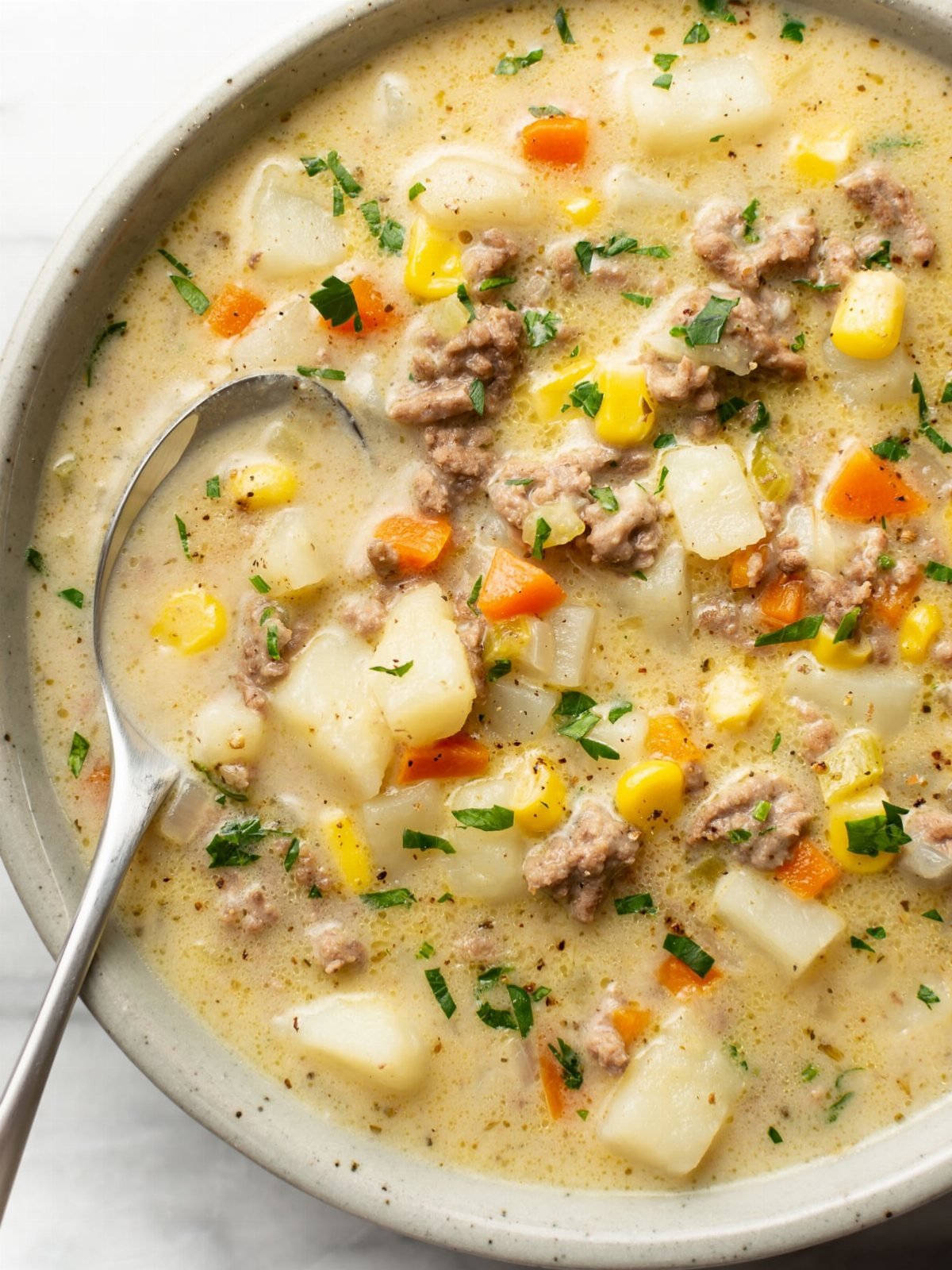 Creamy hamburger soup with ground beef, potatoes, corn, and carrots in a white bowl with a spoon.