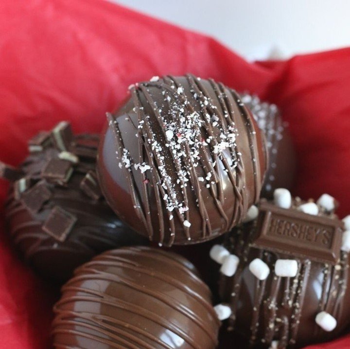 Chocolate hot chocolate bombs with peppermint sprinkles and chocolate drizzle in red tissue paper.