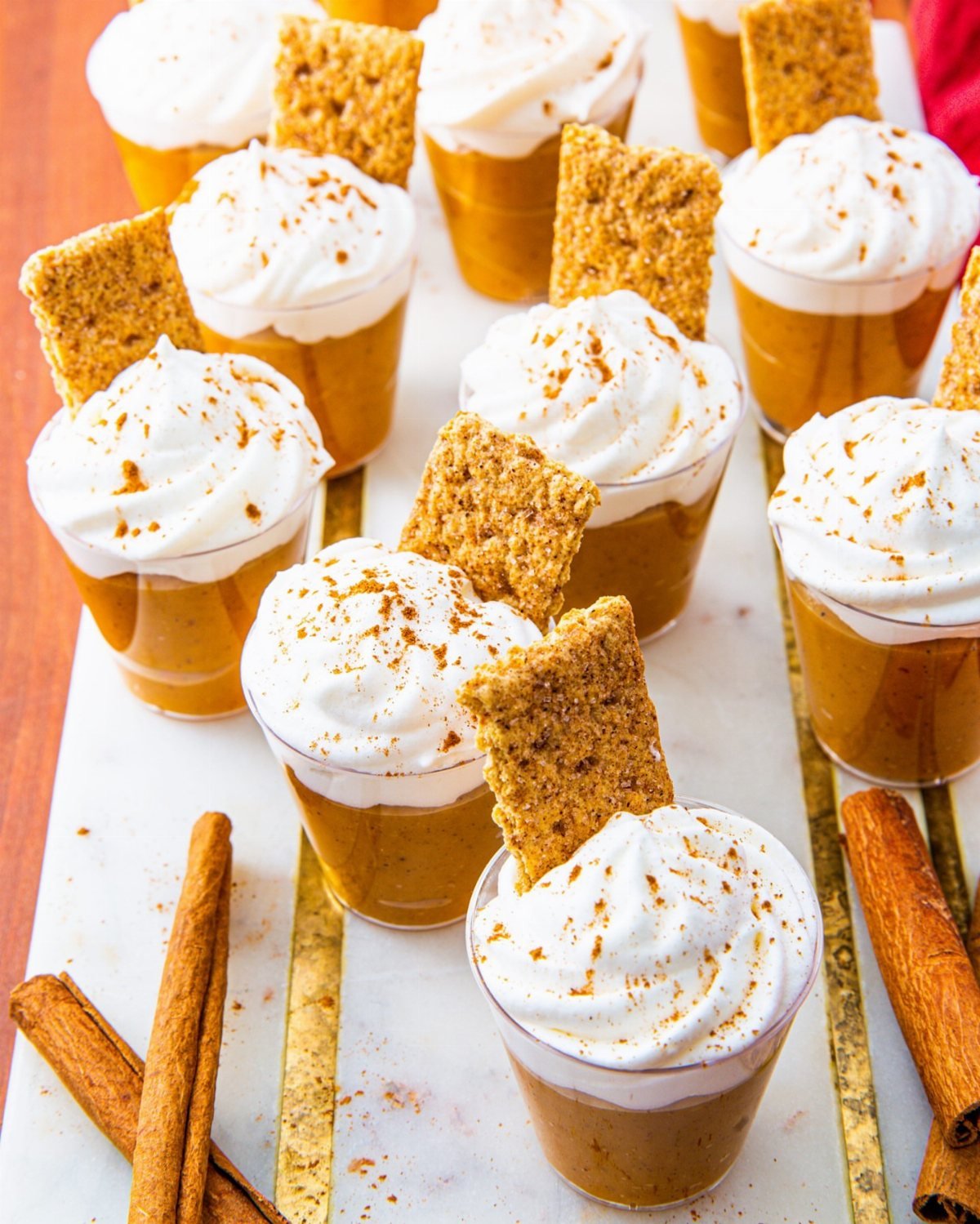 Small glasses of pumpkin pudding topped with whipped cream and graham cracker pieces on a marble tray.
