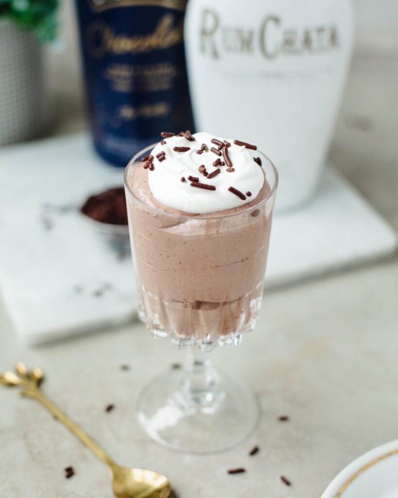 Chocolate pudding shot in a glass goblet topped with whipped cream and chocolate sprinkles on marble.
